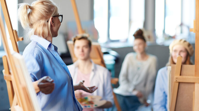 Teacher,Pointing,At,Her,Painting,On,Easel,While,Explaining,Her